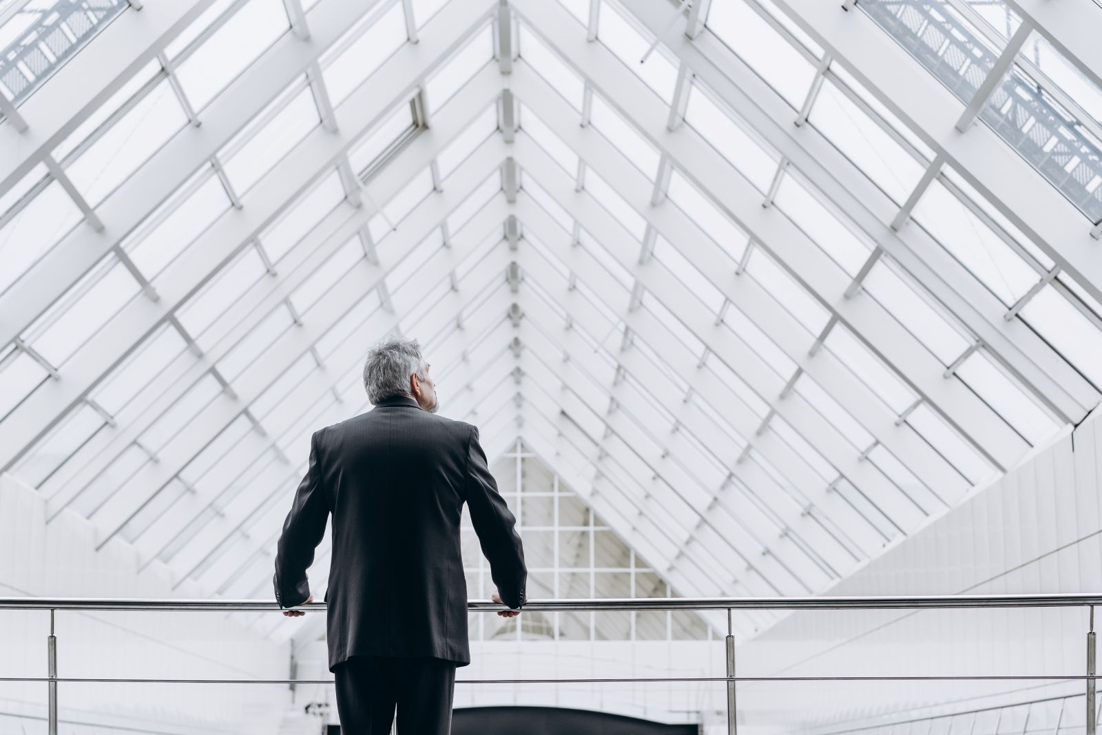 Older executive gazes over balcony inside atrium of large office building.